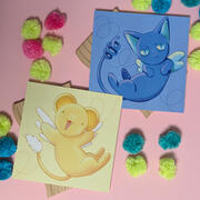 A photo of two mini prints featuring art by Ayumutan Art, inspired by Kero and Suppi from Cardcaptor Sakura