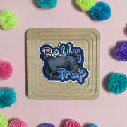 A sticker featuring a grey cat rolling on its back with a mischievous expression, and holographic text saying "belly trap" in the background